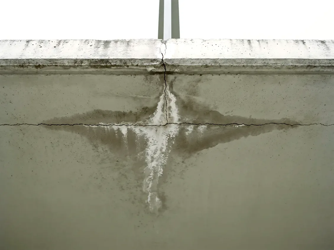 The underside of a concrete balcony slab showing a hairline crack, white efflorescence and a spreading damp stain