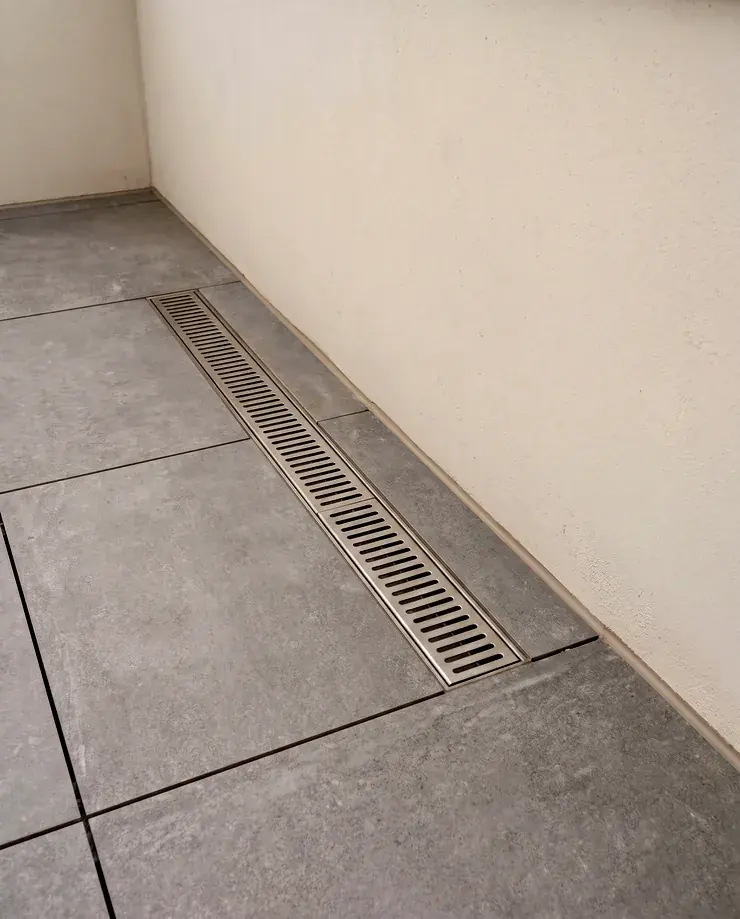 Detail of a newly tiled balcony edge meeting a rendered upstand with a slim stainless drainage channel