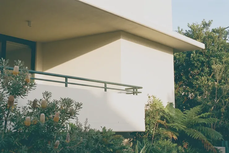 The corner of a freshly rendered apartment building with a deep green handrail and native planting